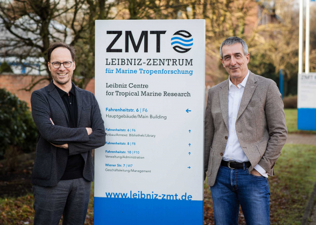 Two men stand to the left and right of a company sign of the Leibniz Centre for Tropical Marine Research (ZMT)