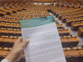 Eine Hand h&auml;lt einen Policy Brief zu nachhaltigen &Auml;stuar- und K&uuml;stengebieten vor den Sitzreihen eines gro&szlig;en, leeren Plenarsaals.