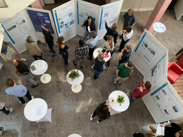 A group of people are gathered in a bright indoor atrium for a professional event or conference.