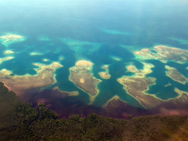 Luftaufnahme einer tropischen Küstenlandschaft mit zahlreichen kleinen Inseln und Lagunen, umgeben von türkisblauem bis tiefblauem Meer.