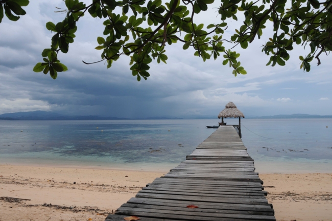 Ein langer Holzsteg führ zu einer kleine strohbedeckten Hütte ins Meers in Manado, Indonesien