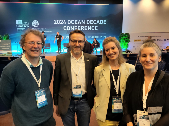 Vier Personen stehen vor einem großen Bildschirm mit den Worten "Ocean Decade Conference".