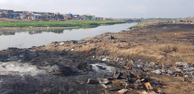 Elektroschrott in Agbogbloshie in Accra, Ghana, im Hintergrund sind Blechhütten zu sehen